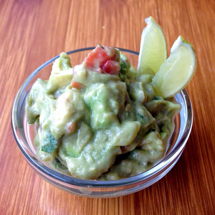 Mexican Guacamole in a bowl is lime wedges