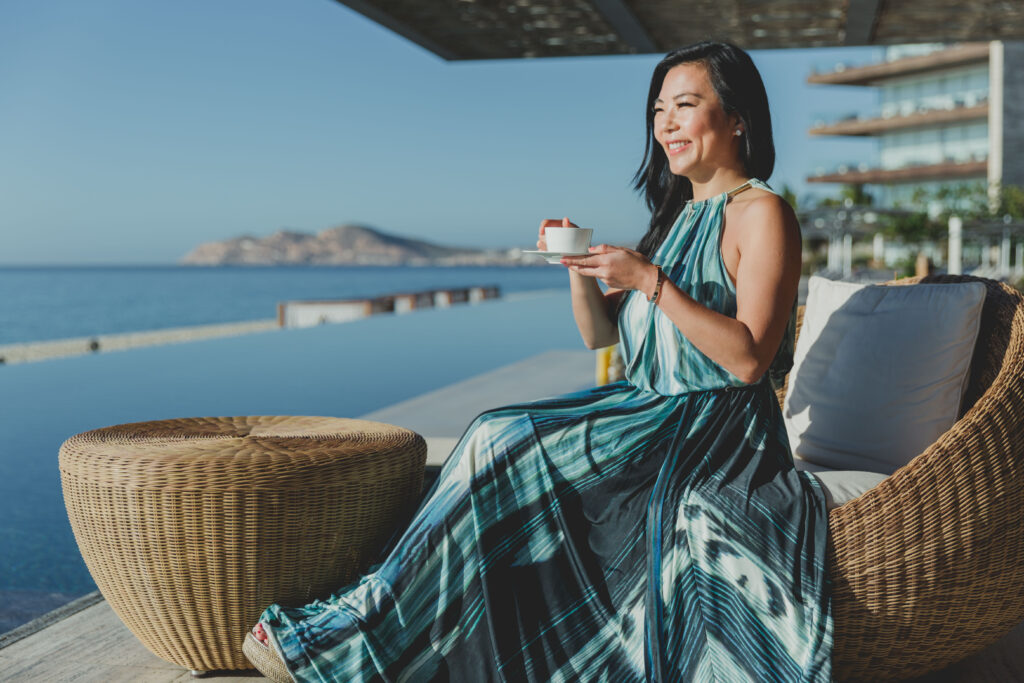 The travel and food blogger Tinger is sitting on a wicker chair at the Solaz resort in Cabo, Mexico and looking at the ocean while drinking tea.
