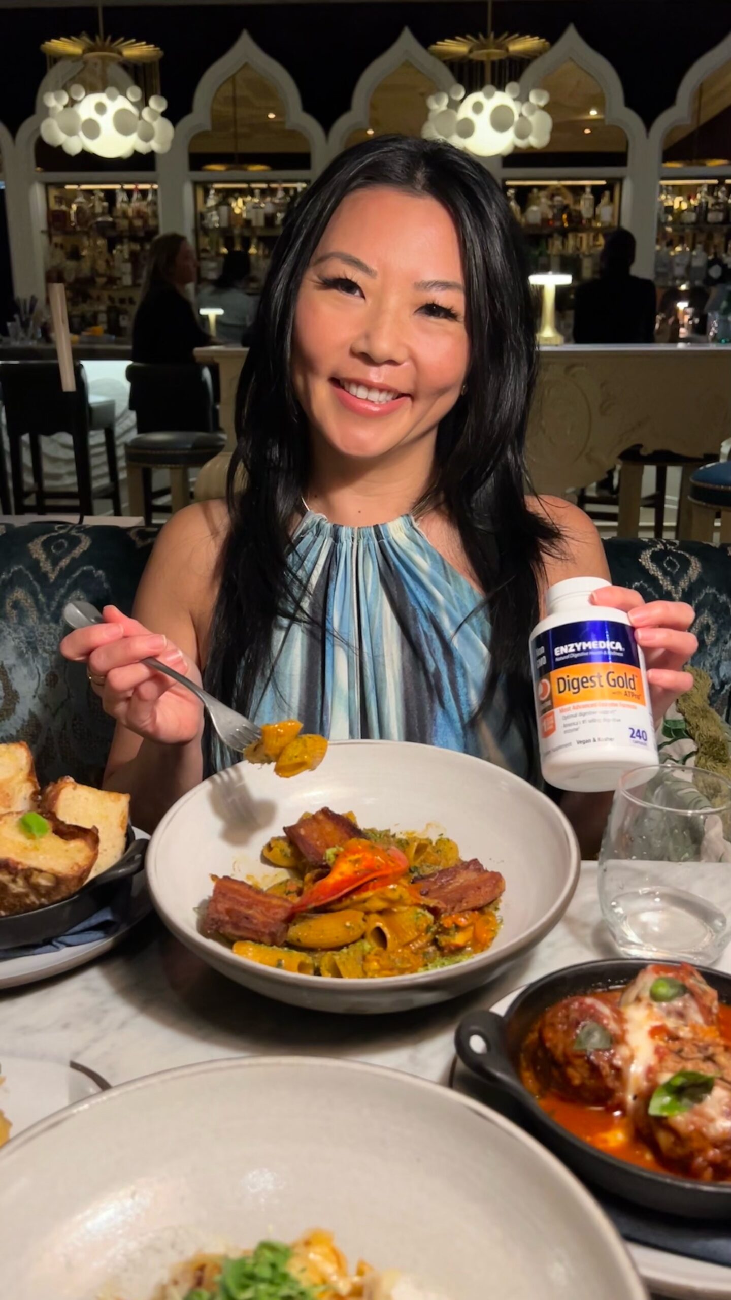 Travel and Food Blogger Tinger Hseih holding a bottle of Enzymedica Digest Gold while eating at an Italian restaurant